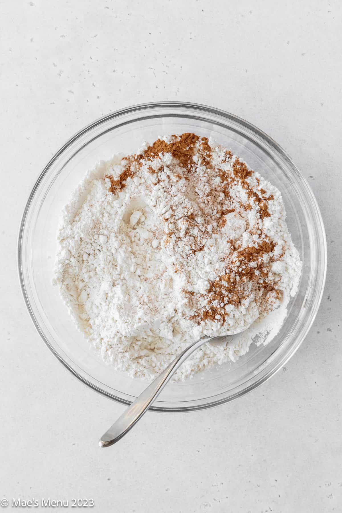 A glass bowl of flour and cinnamon with a spoon.