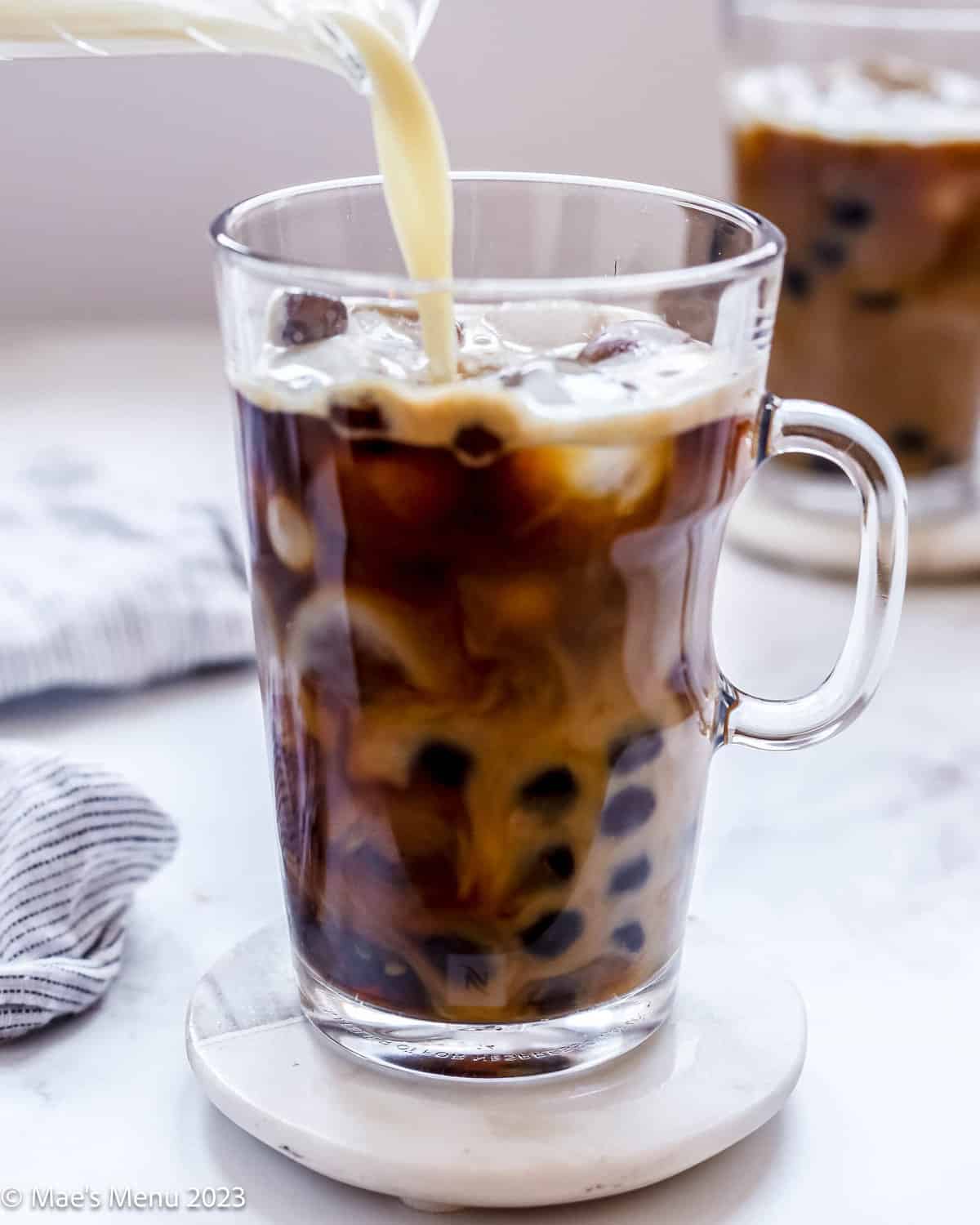 Pouring milk into the glass coffee mug with milk and boba pearls.