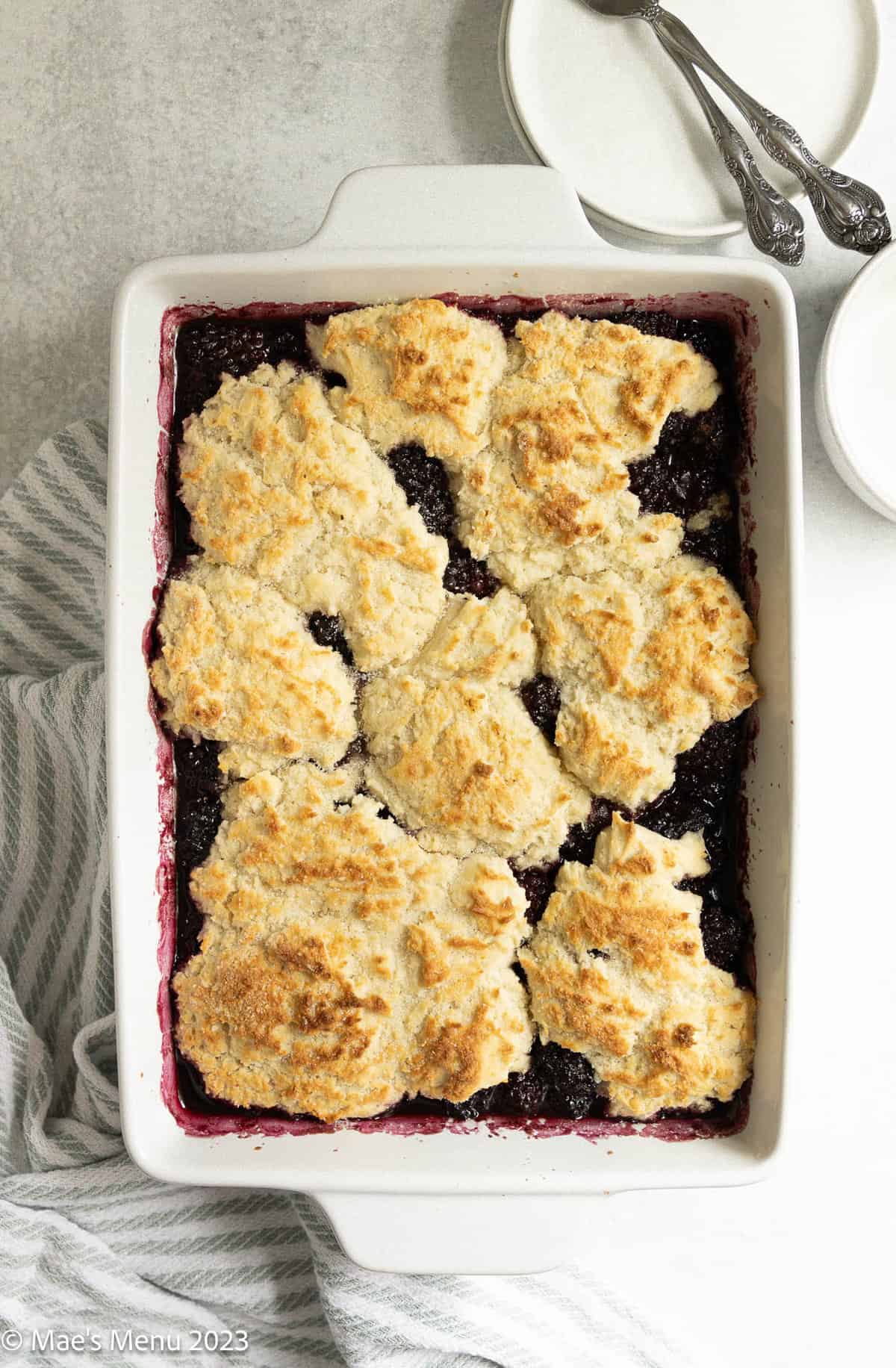 Gluten-free blackberry cobbler on the counter with a dish towel, plates, and a fork.