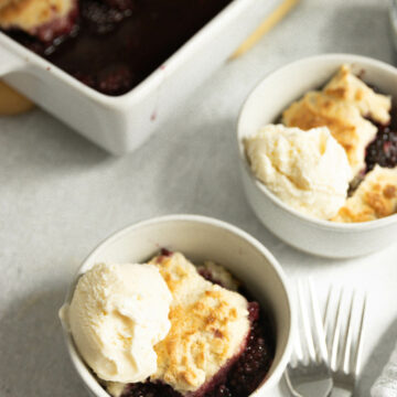 Two small dishes of gluten-free blackberry cobbler on the counter with forks.