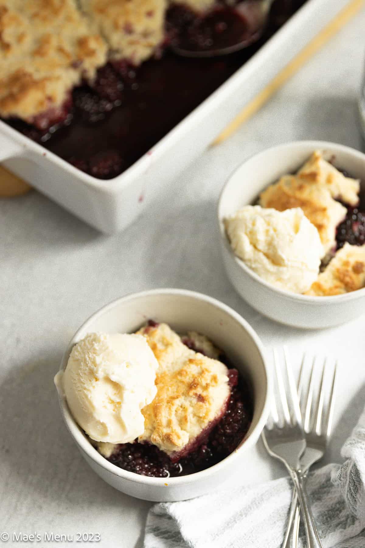 Two small dishes of gluten-free blackberry cobbler on the counter with forks.