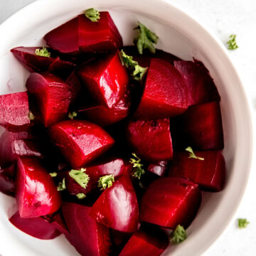 Cooked cut beets in a white bowl with chopped curly parsley.