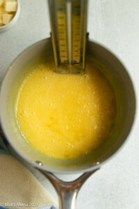 Cooked meyer lemon curd in a sauce pan with a candy thermometer.