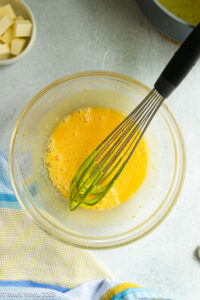 A glass mixing bowl of whisked egg yolks and some hot lemon juice.