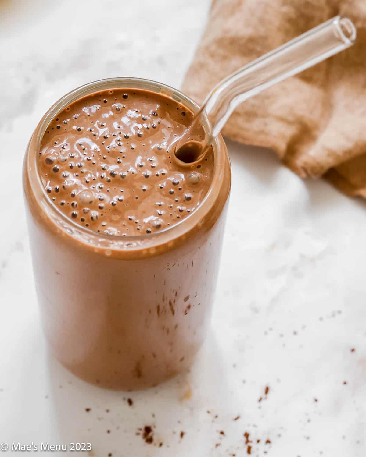 An up-close shot of a glass of mocha protein shakes with a glass straw.