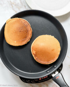 two cooked pancakes on a griddle.