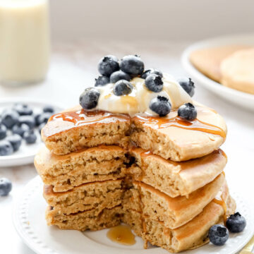 A stack of oat milk pancakes with yogurt, blueberries, and syrup.