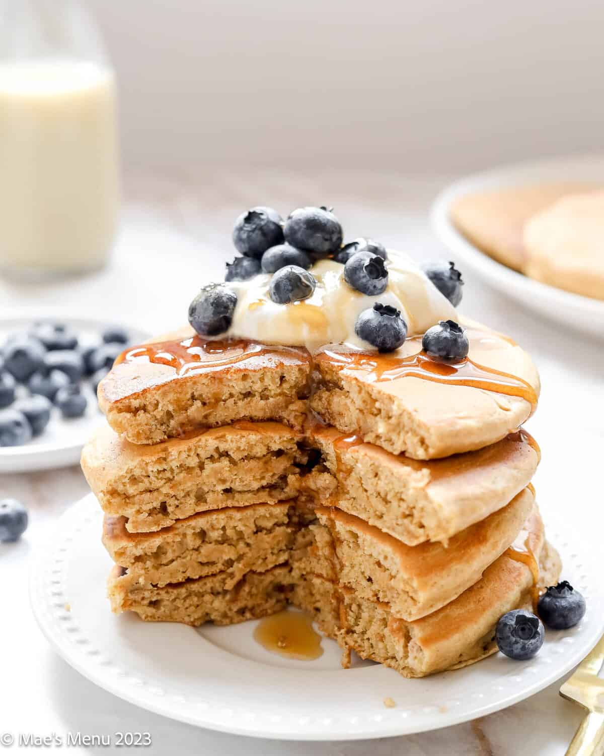 A stack of oat milk pancakes with yogurt, blueberries, and syrup.