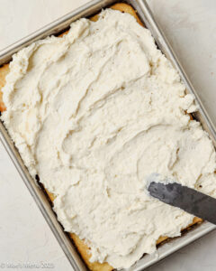 A frosted pineapple poke cake with a frosting spatula.