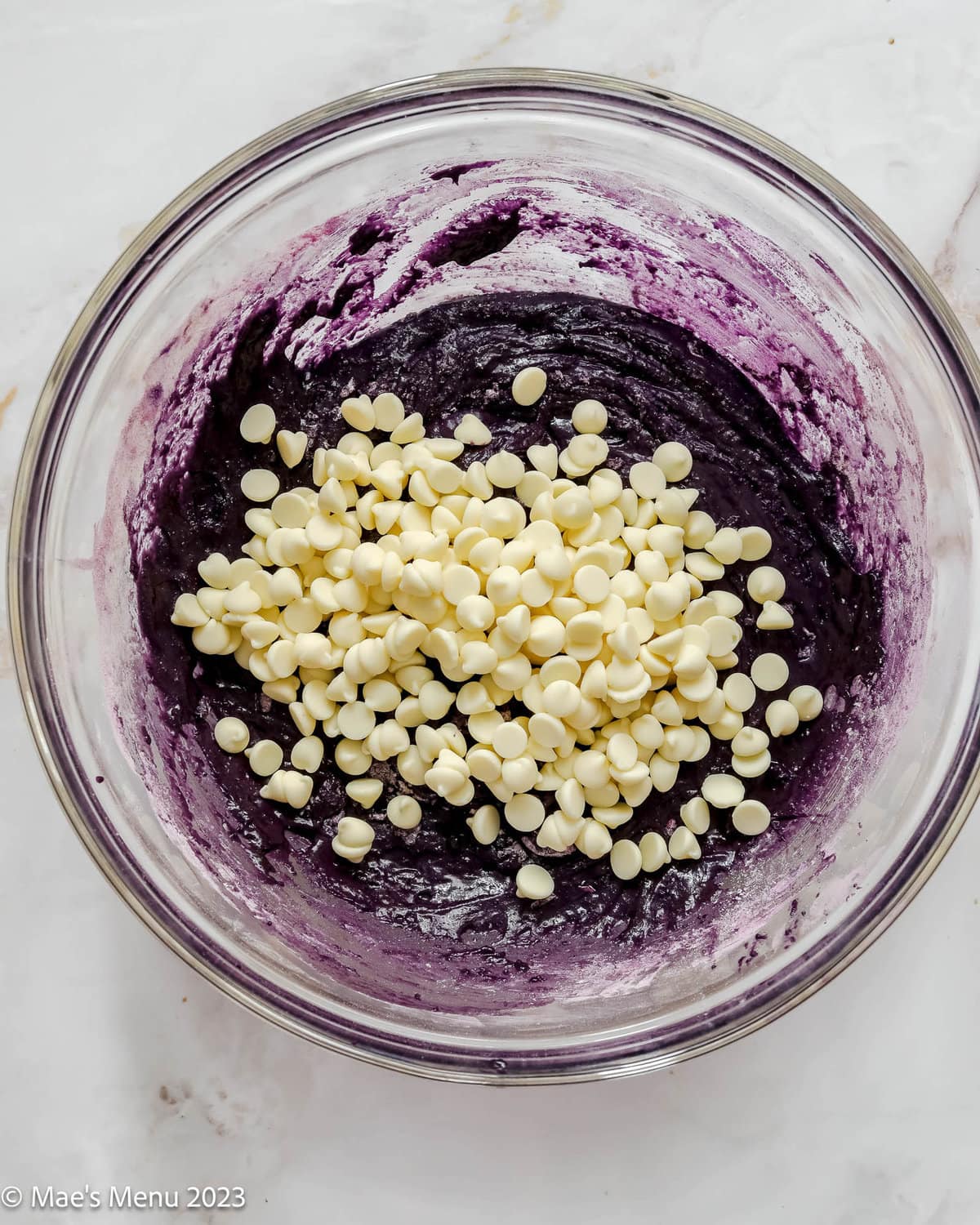 A glass mixing bowl with ube brownie batter and white chocolate chips.