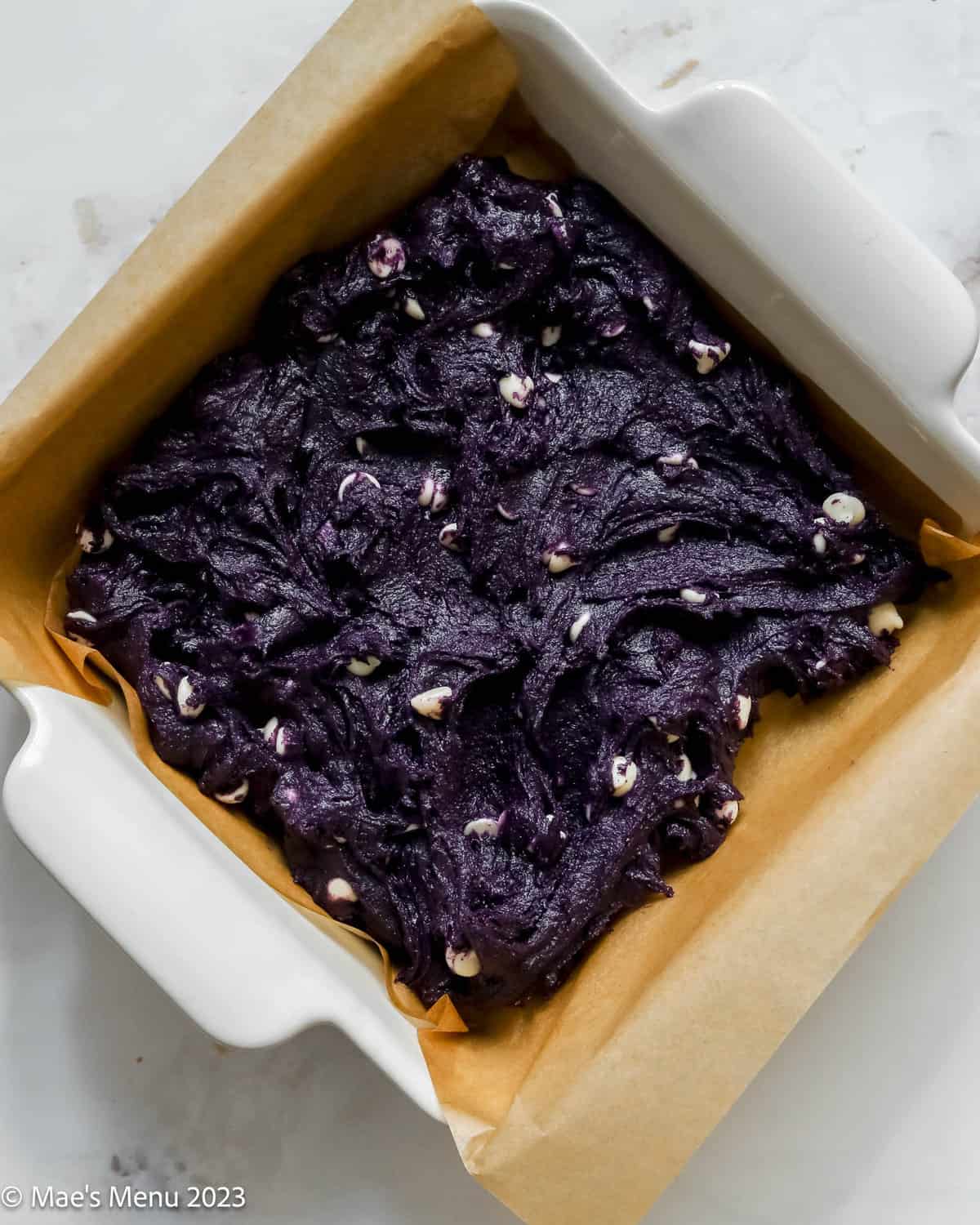 An overhead shot of a pan of ube brownie batter in a parchment paper lined baking dish.