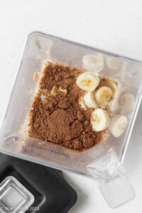 An overhead shot of a blender with milk, cocoa powder, and bananas.