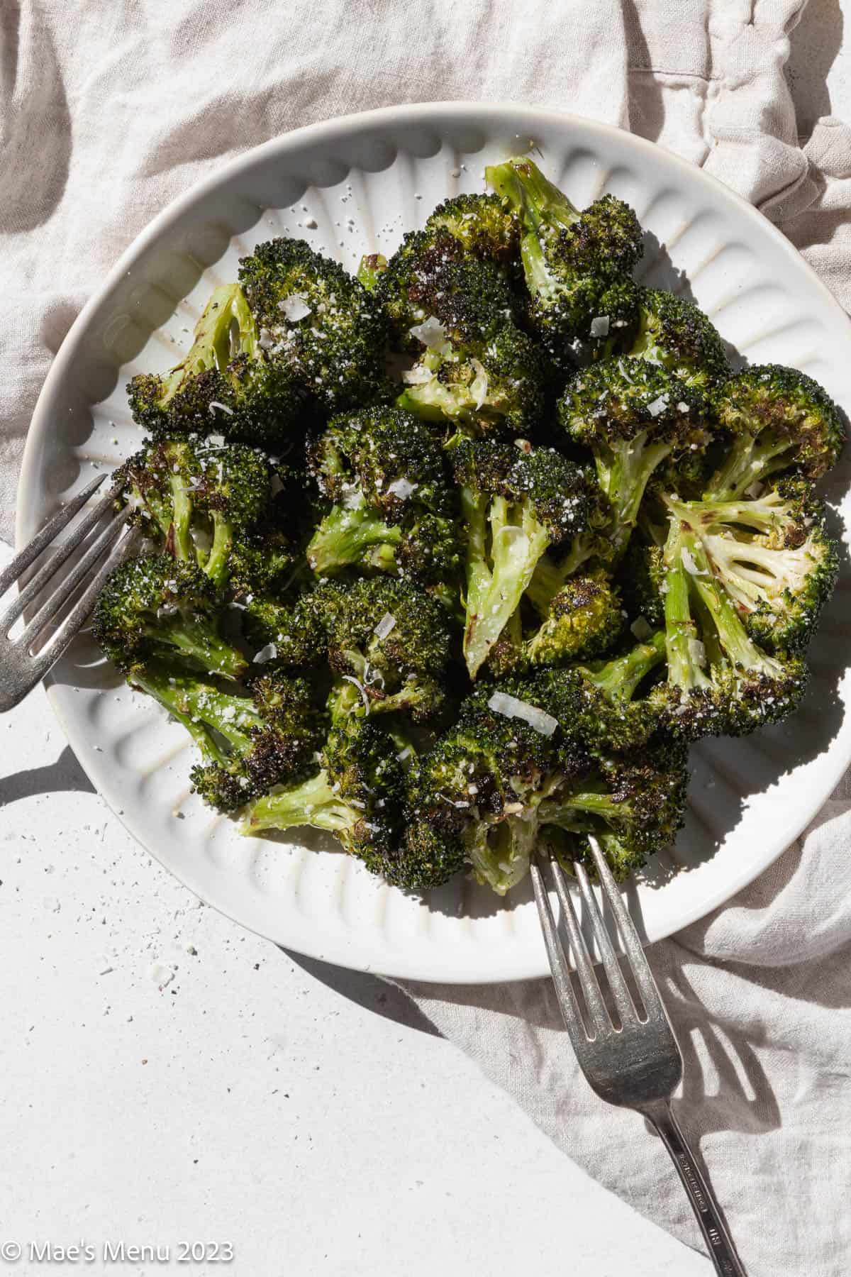 Overhead shot of a white plate of roasted broccoli with two forks.