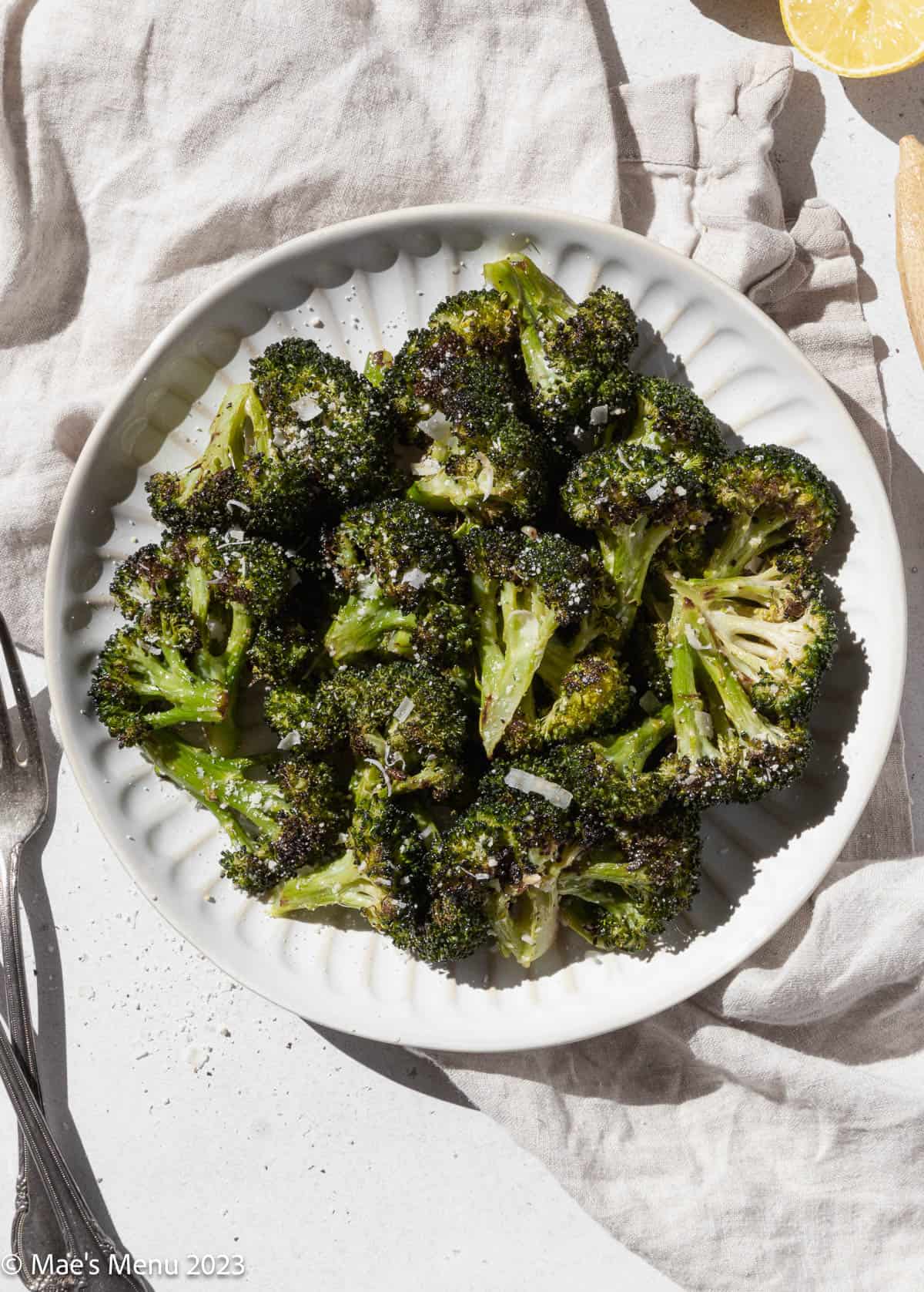 Overhead shot of a white plate of roasted broccoli on a dish cloth with forks and napkins.