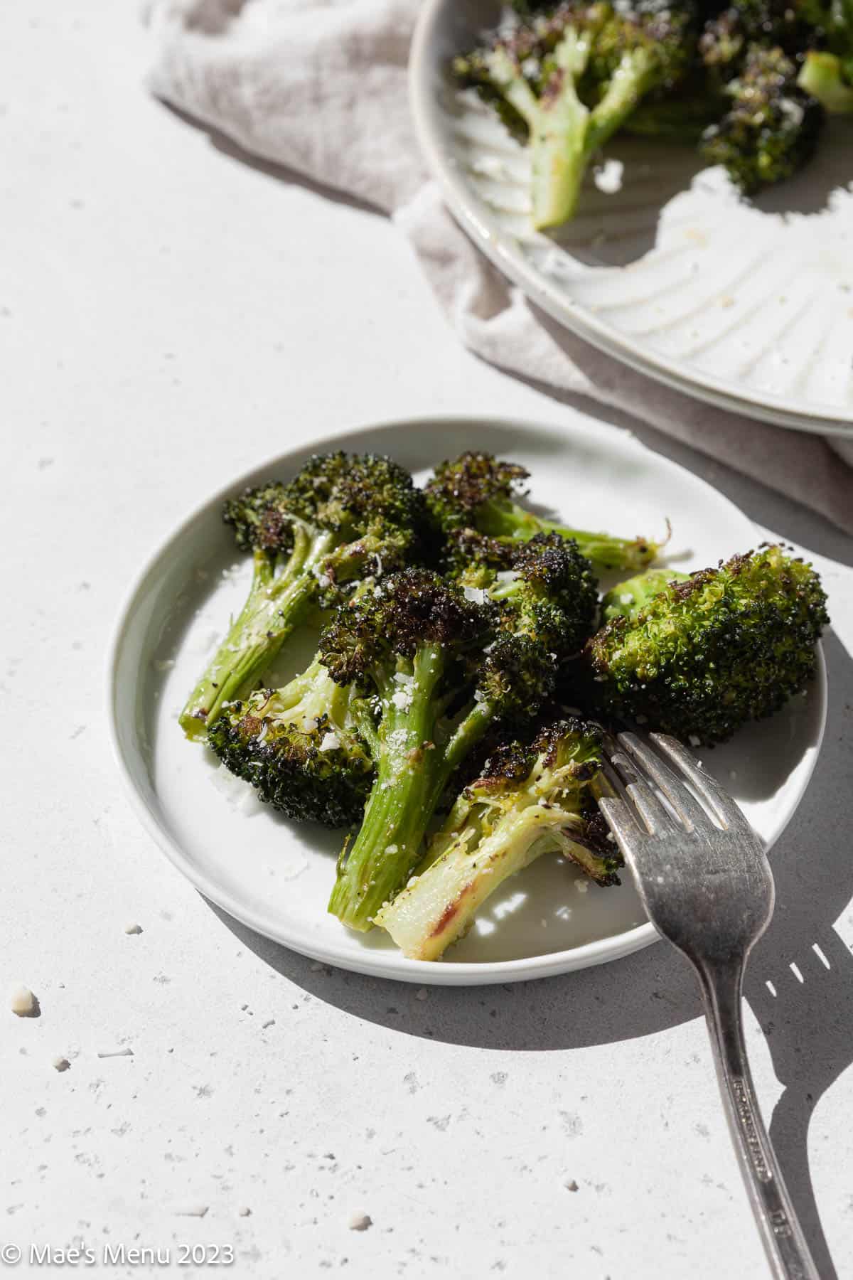 Closeup shot of a small plate of roasted broccoli with a fork.