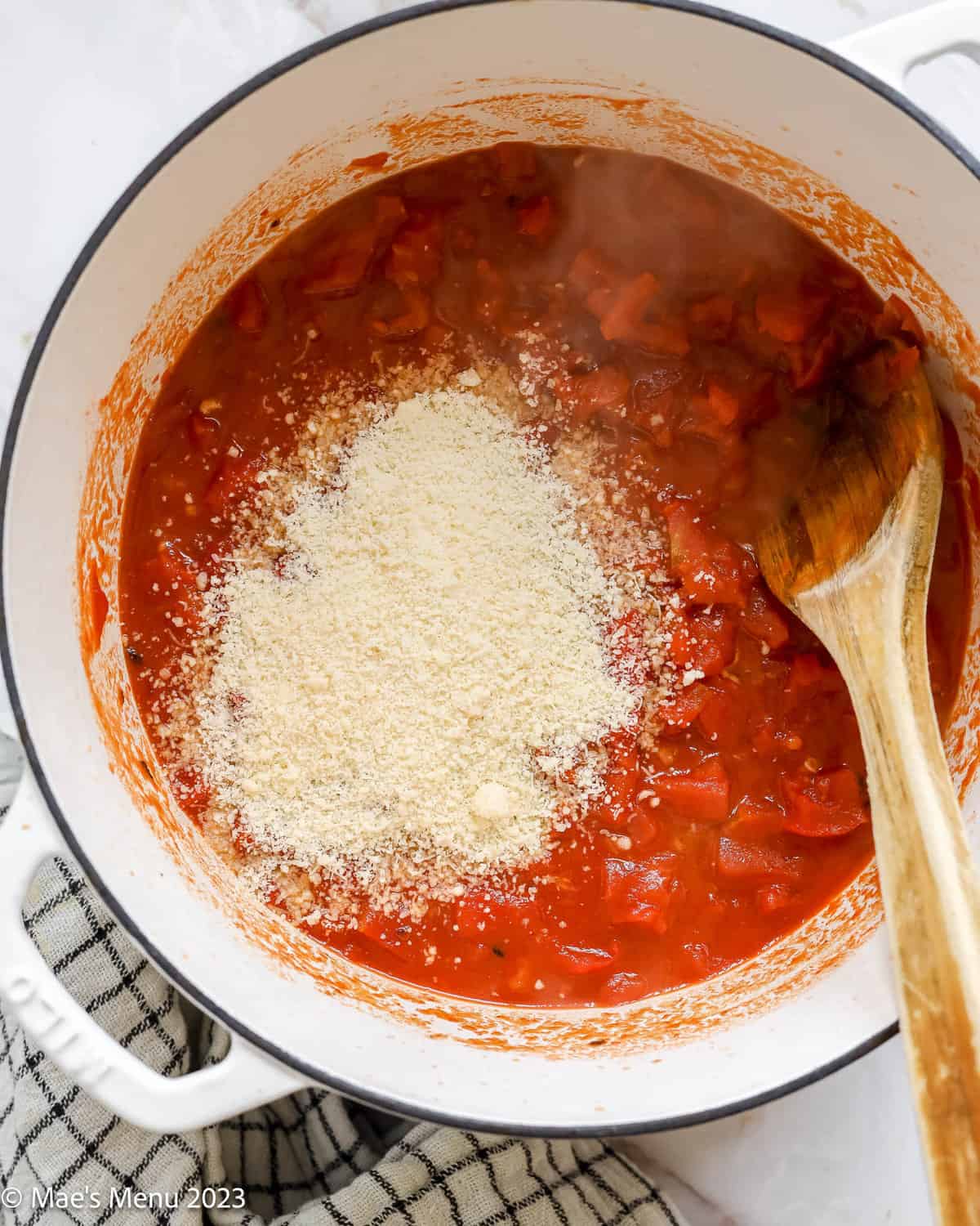 A large pot of simmering tomatoes with grated parmesan cheese.