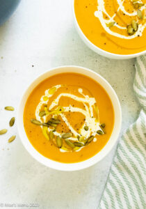 Two bowls of vegan butternut squash soup on the counter with a napkin.