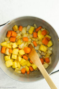 Apples, carrots, and onions sauteing in a pot.