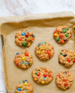Partial overhead shot of oatmeal M&M cookies on parchment paper and baking tray
