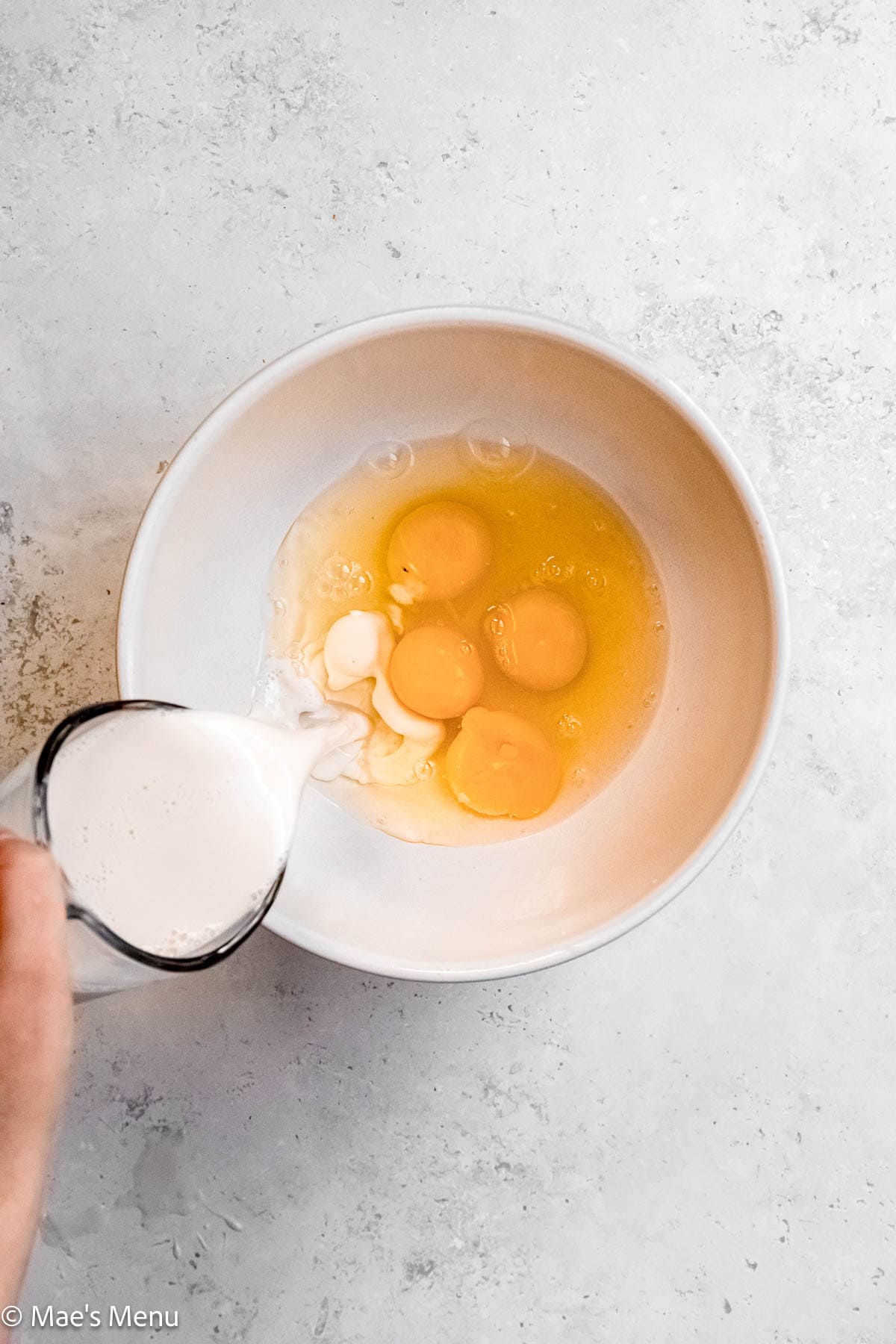 Pouring milk into a large mixing bowl with eggs.