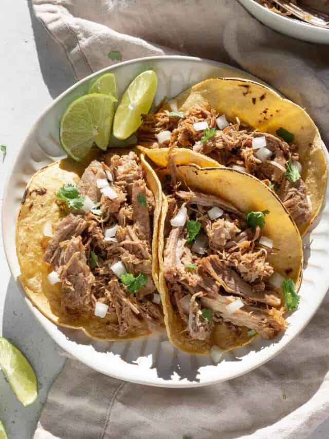Three pork carnitas tacos on a plate with limes.