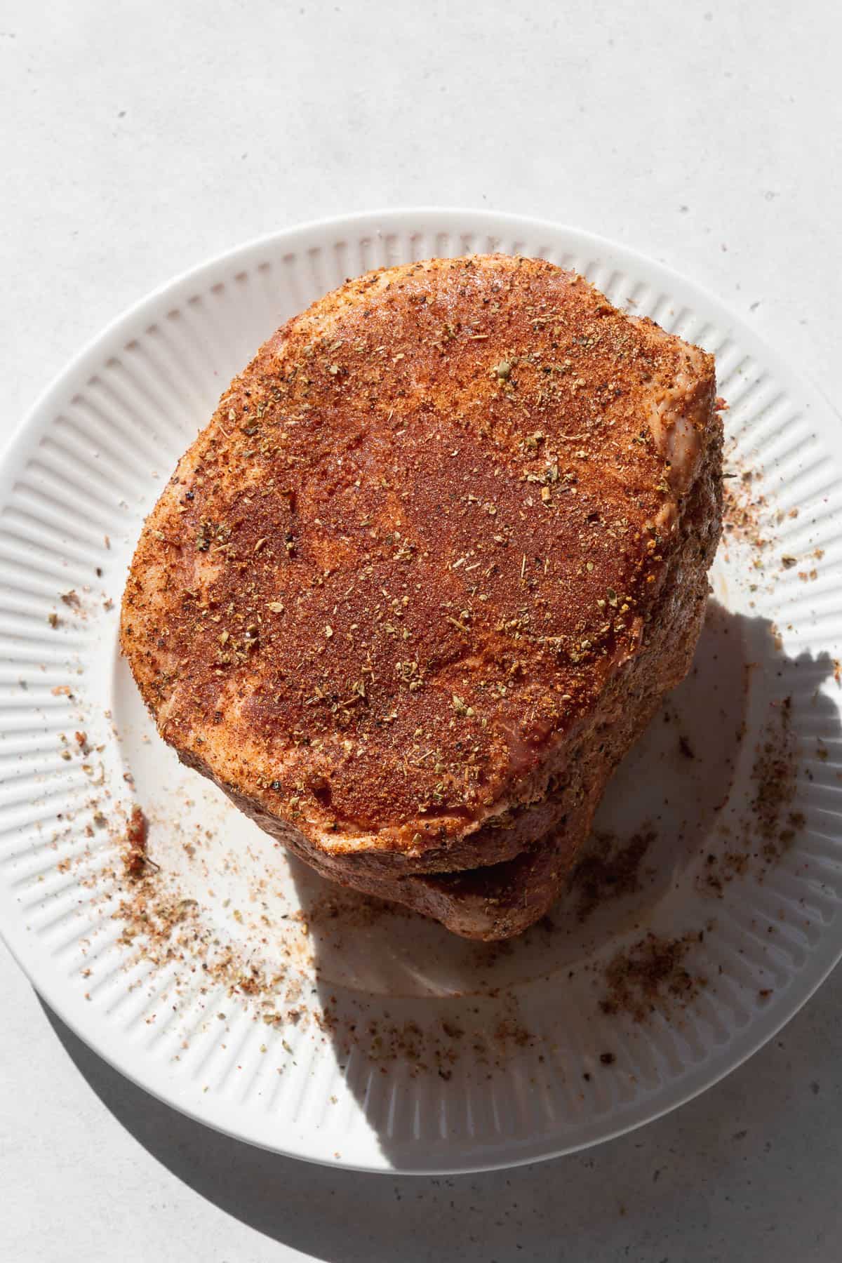 pork covered in dry rub spices sitting on a white plate. 