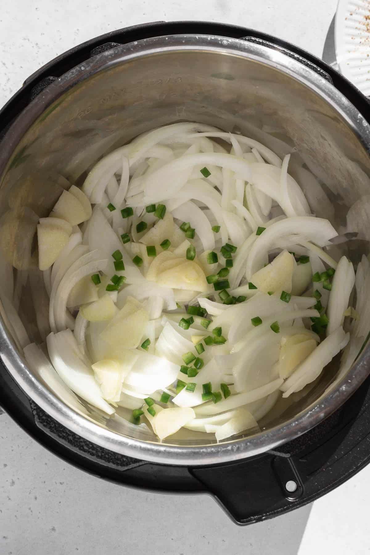 Slices of onion, garlic, and jalapeño in the bottom of a slow cooker.