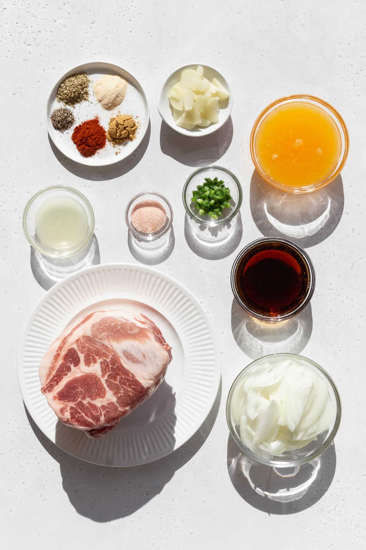 All the ingredients to make pork carnitas sitting on white countertop. 
