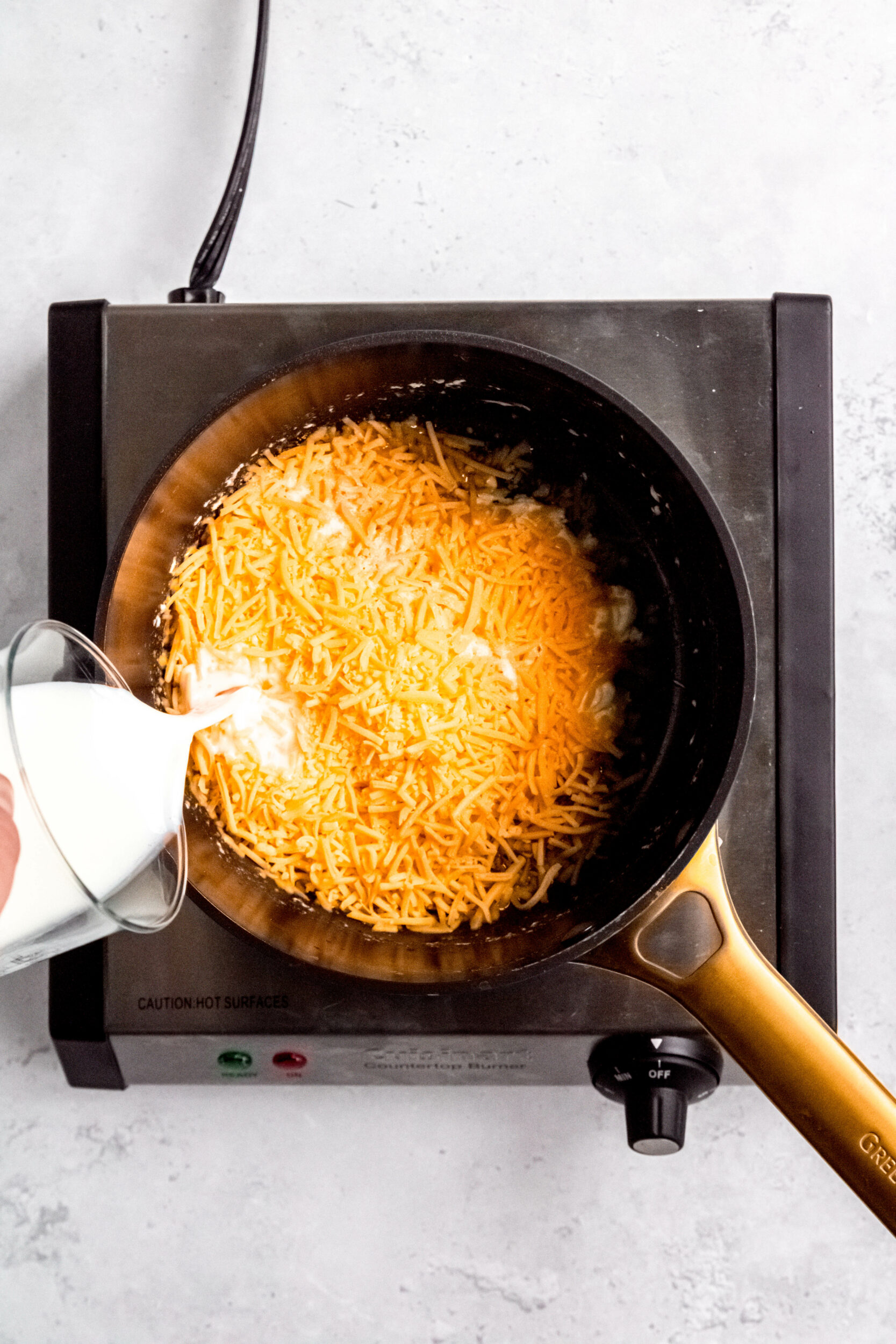 Pouring the milk into the sauce pan with the cheese.