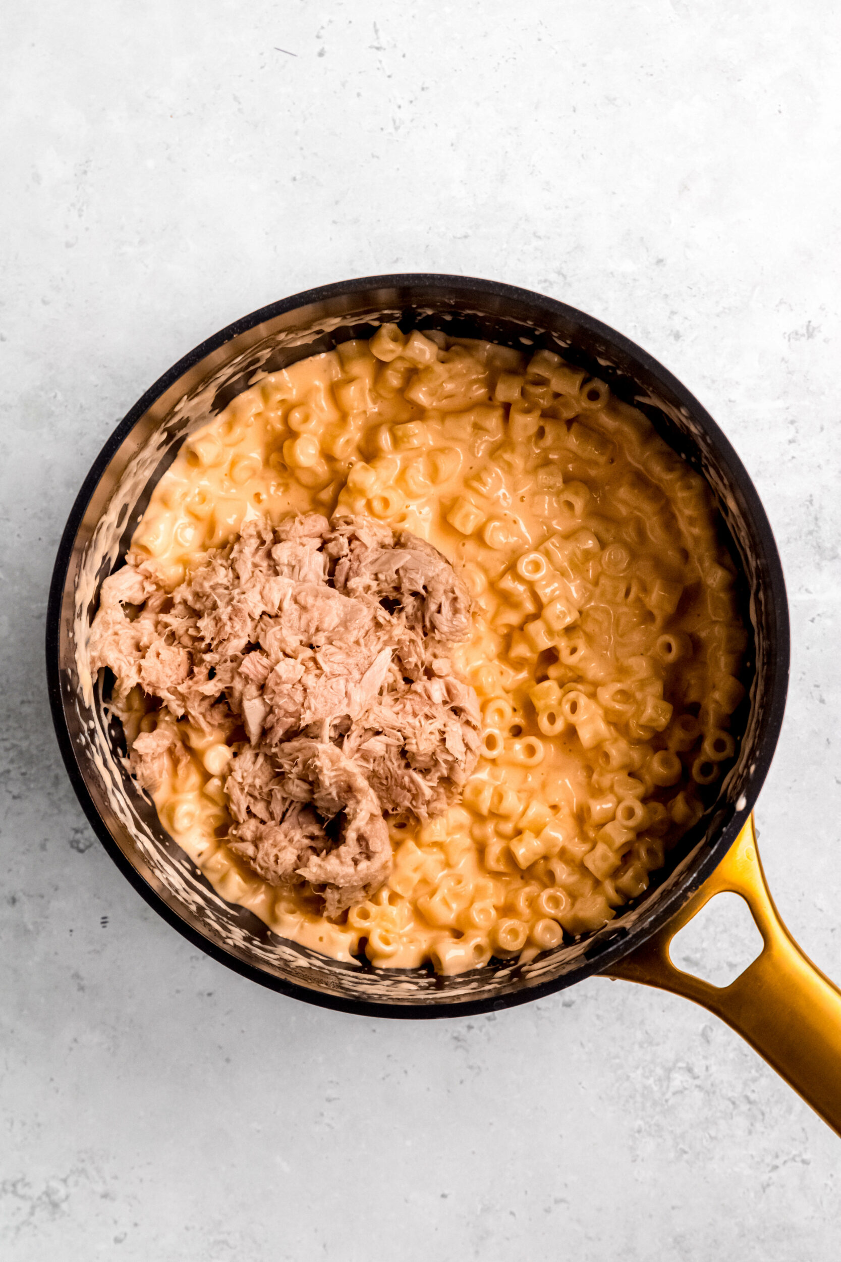 A sauce pan of mac and cheese with flaked tuna added.