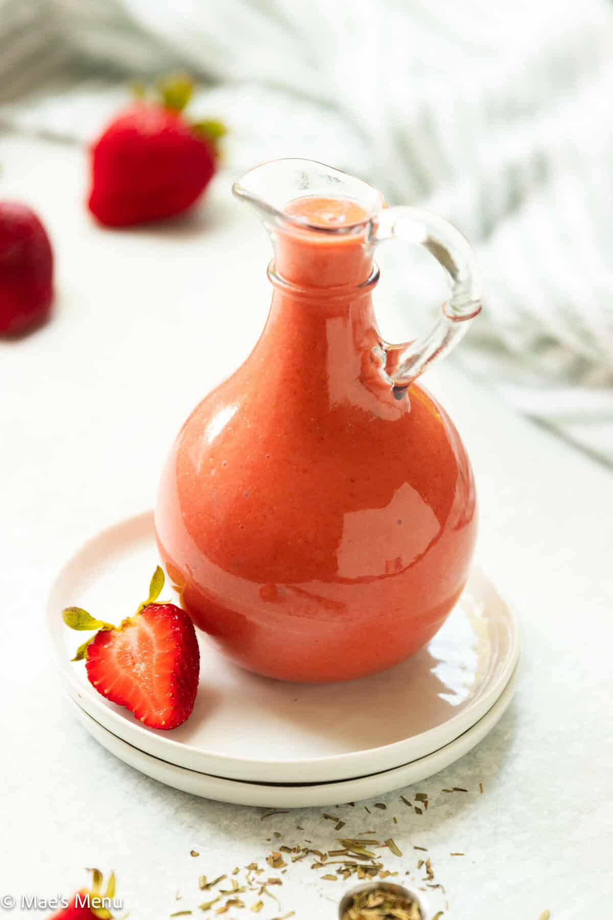 A small dressing bottle of strawberry vinaigrette on two white plates on the counter.