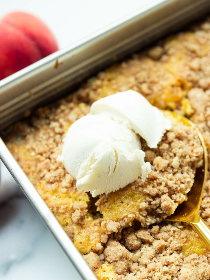 An elevated shot of peach dump cake in a pan with two scoops of ice cream.