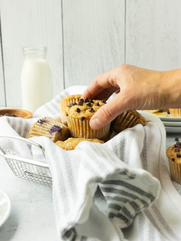 A hand grabbing a muffin from a basket.