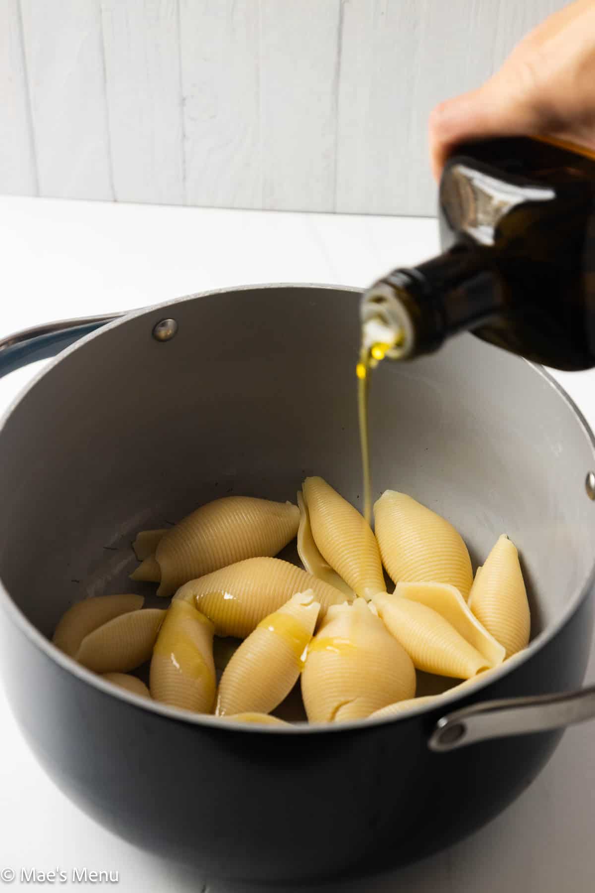 Drizzling the cooked pasta with olive oil.