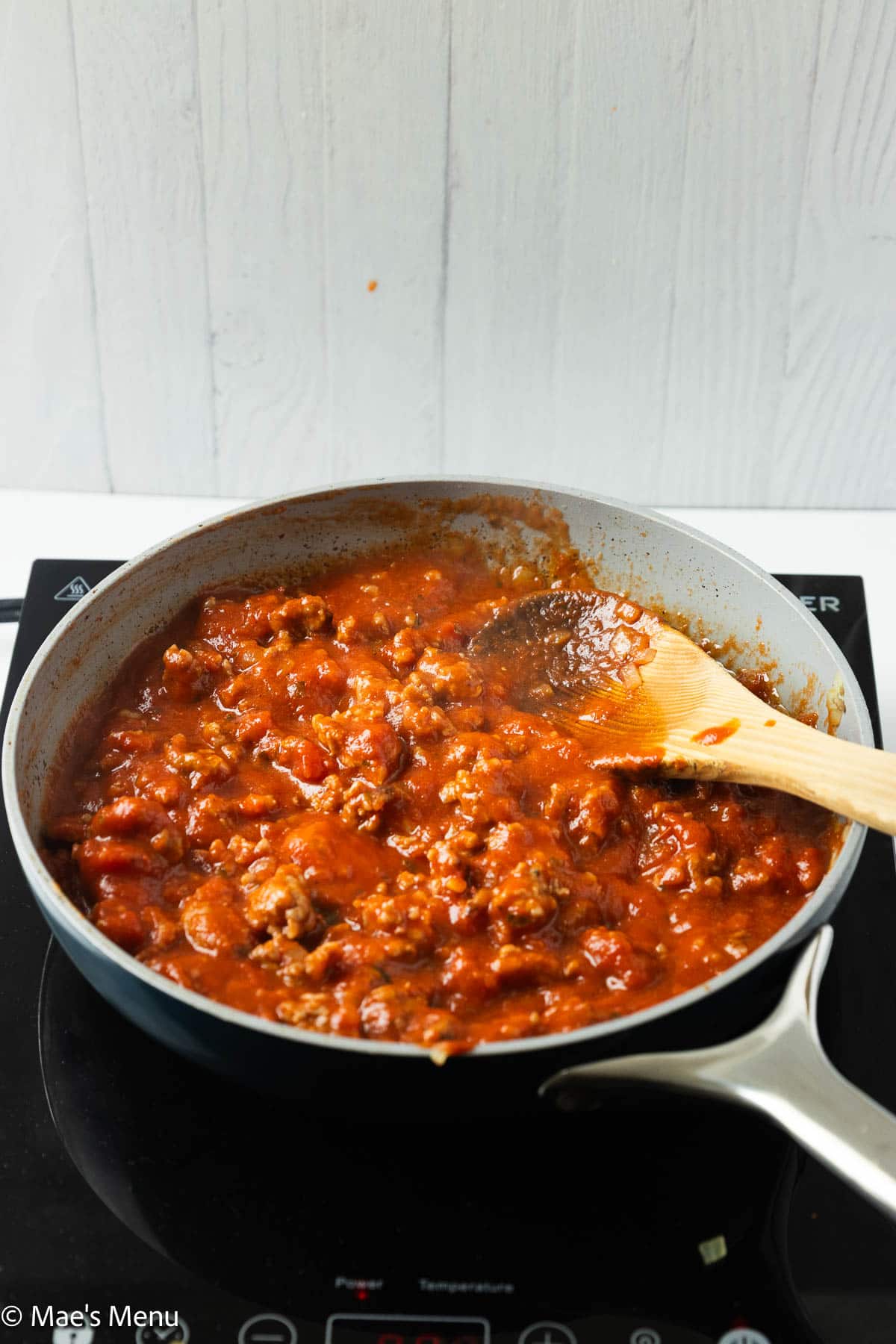 The sausage marinara sauce simmering in a skillet with a wooden spoon.