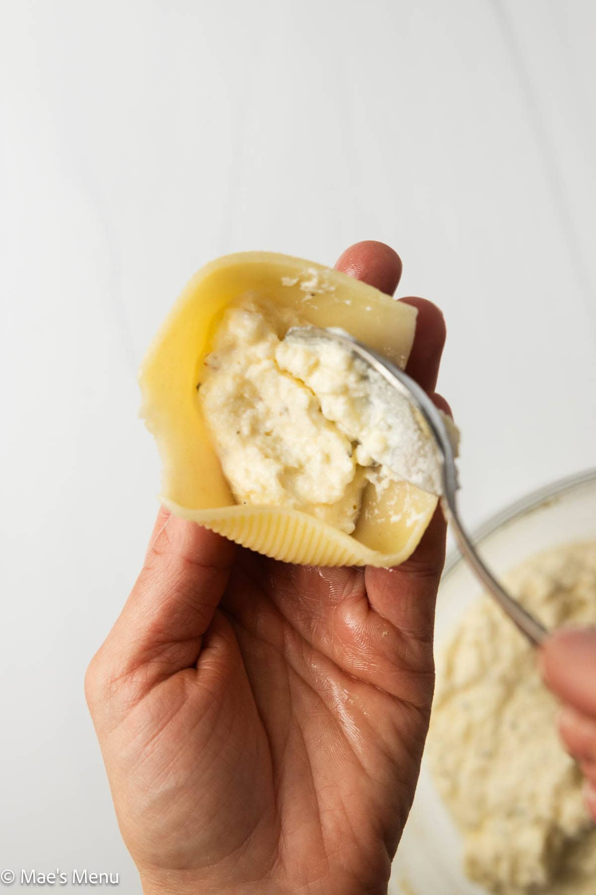A close-up shot of two hands filling the jumbo shells with the ricotta mixture.