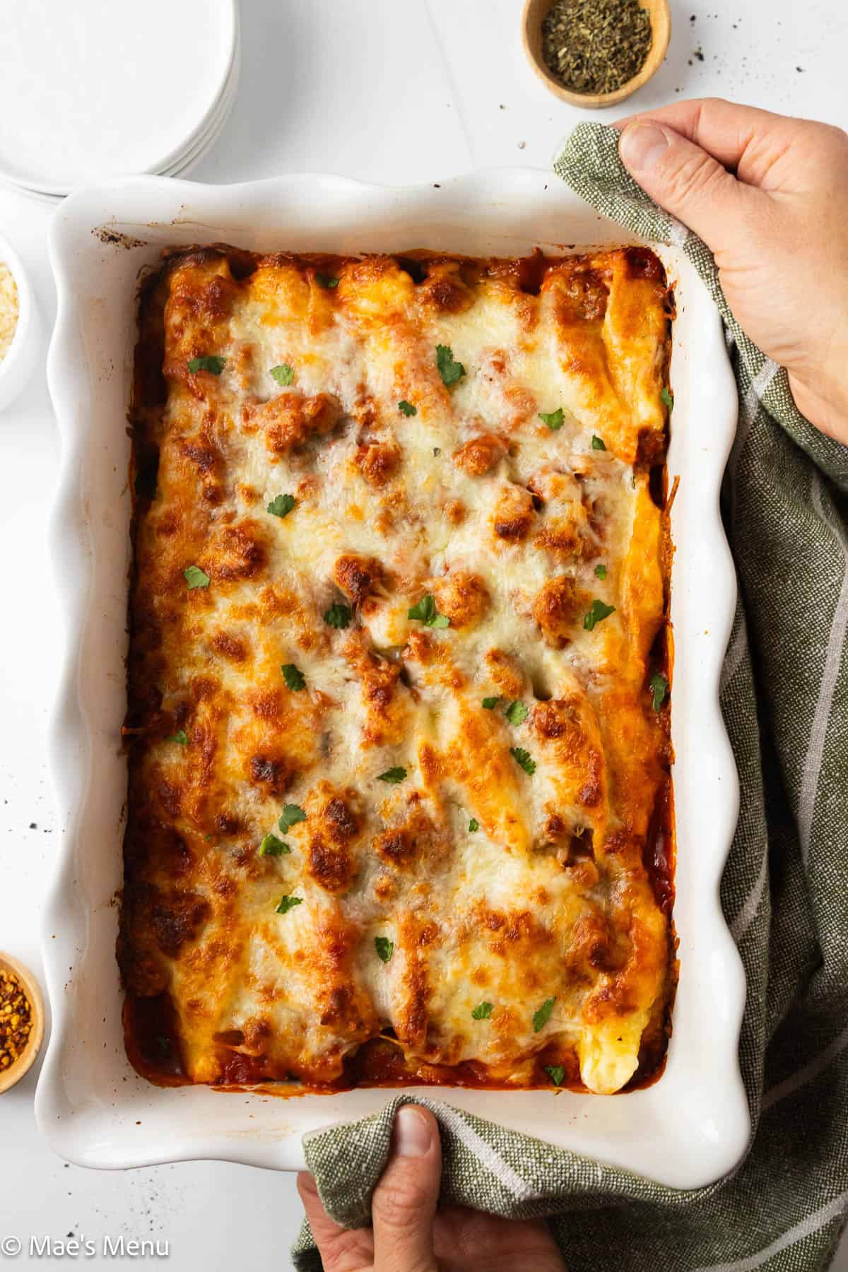 Two hands grabbing the pan of jumbo baked shells.