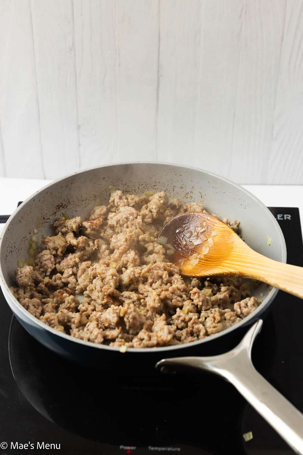 The browned sausage in a skillet with a wooden spoon.