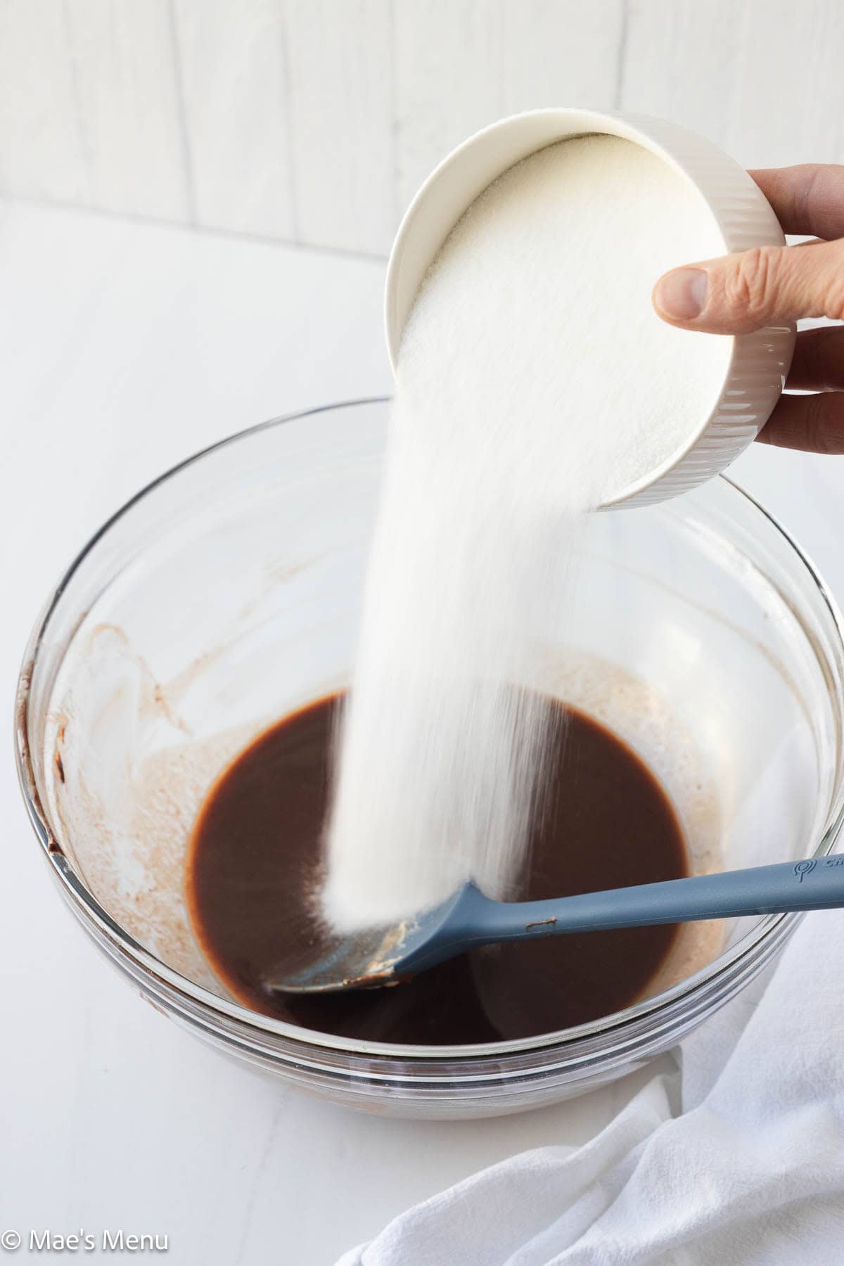 Adding sugar to the melted butter and chocolate in the mixing bowl. 
