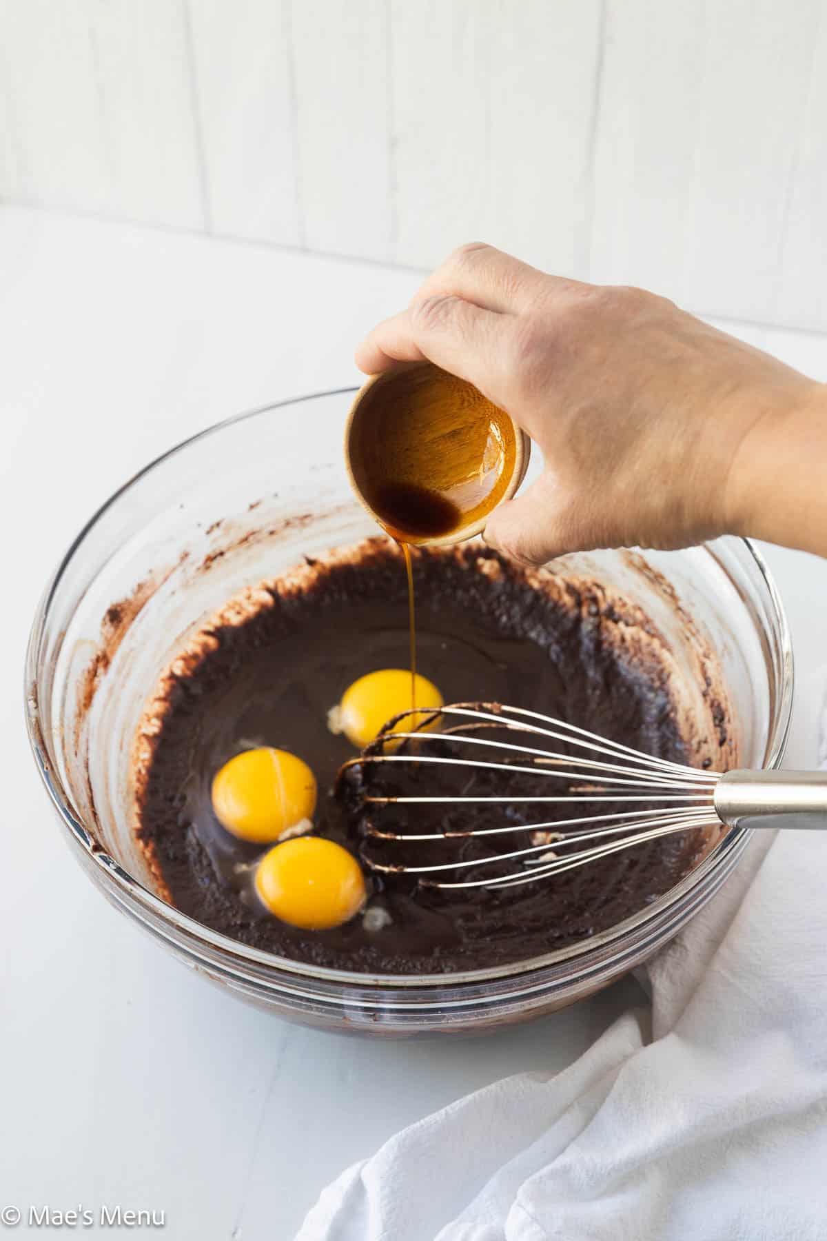 Adding vanilla to the mixing bowl with the chocolate base and eggs.