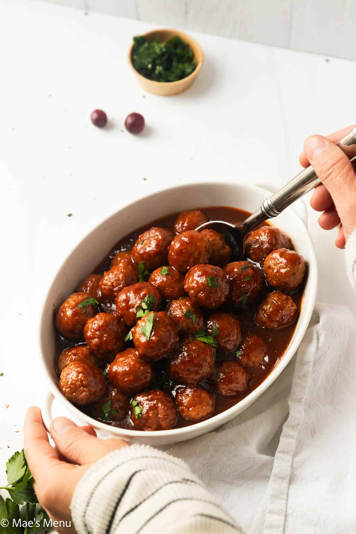 Two hands holding the post of cranberry meatballs to start serving.
