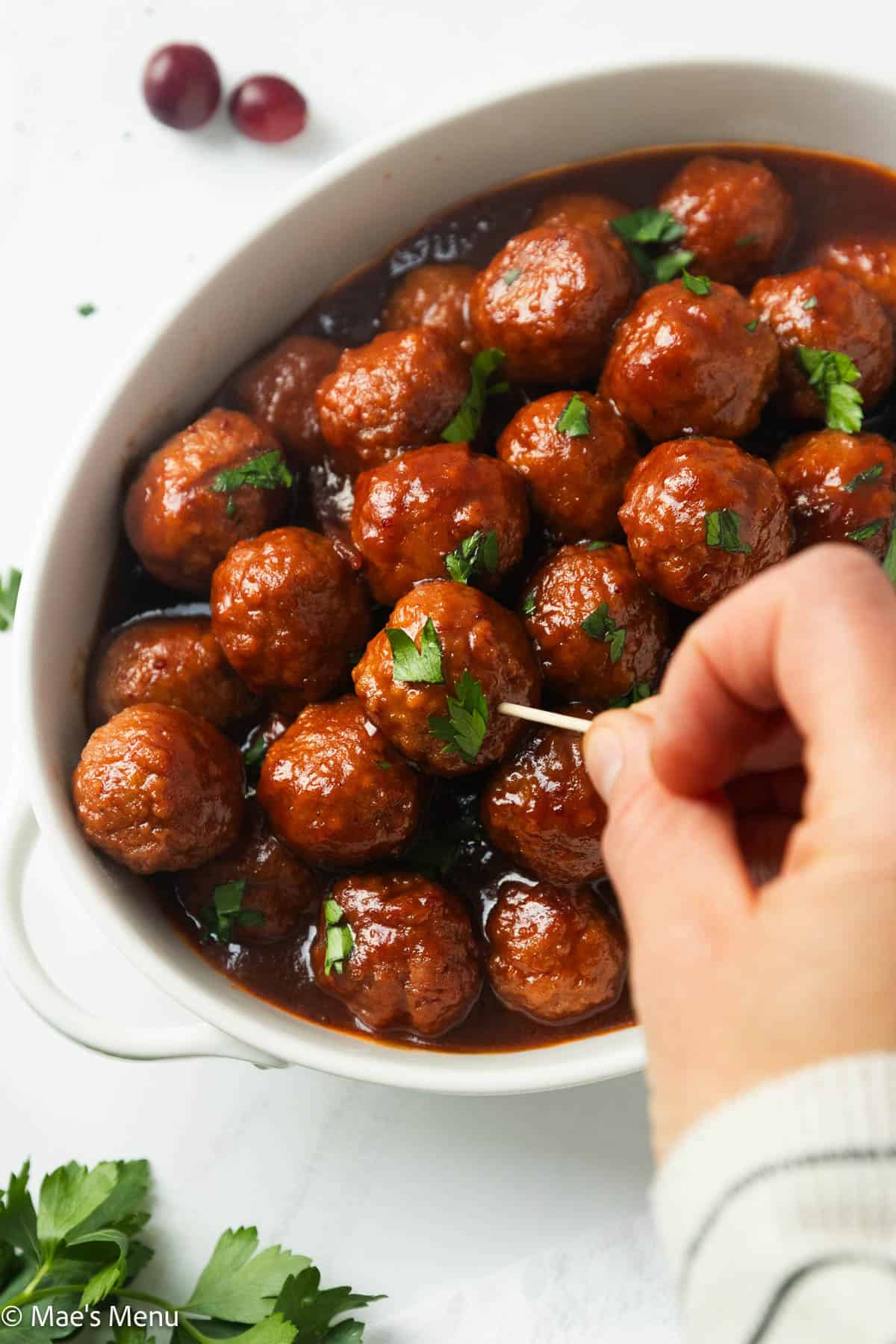 An overhead shot of a hand grabbing a meatball with a toothpick.