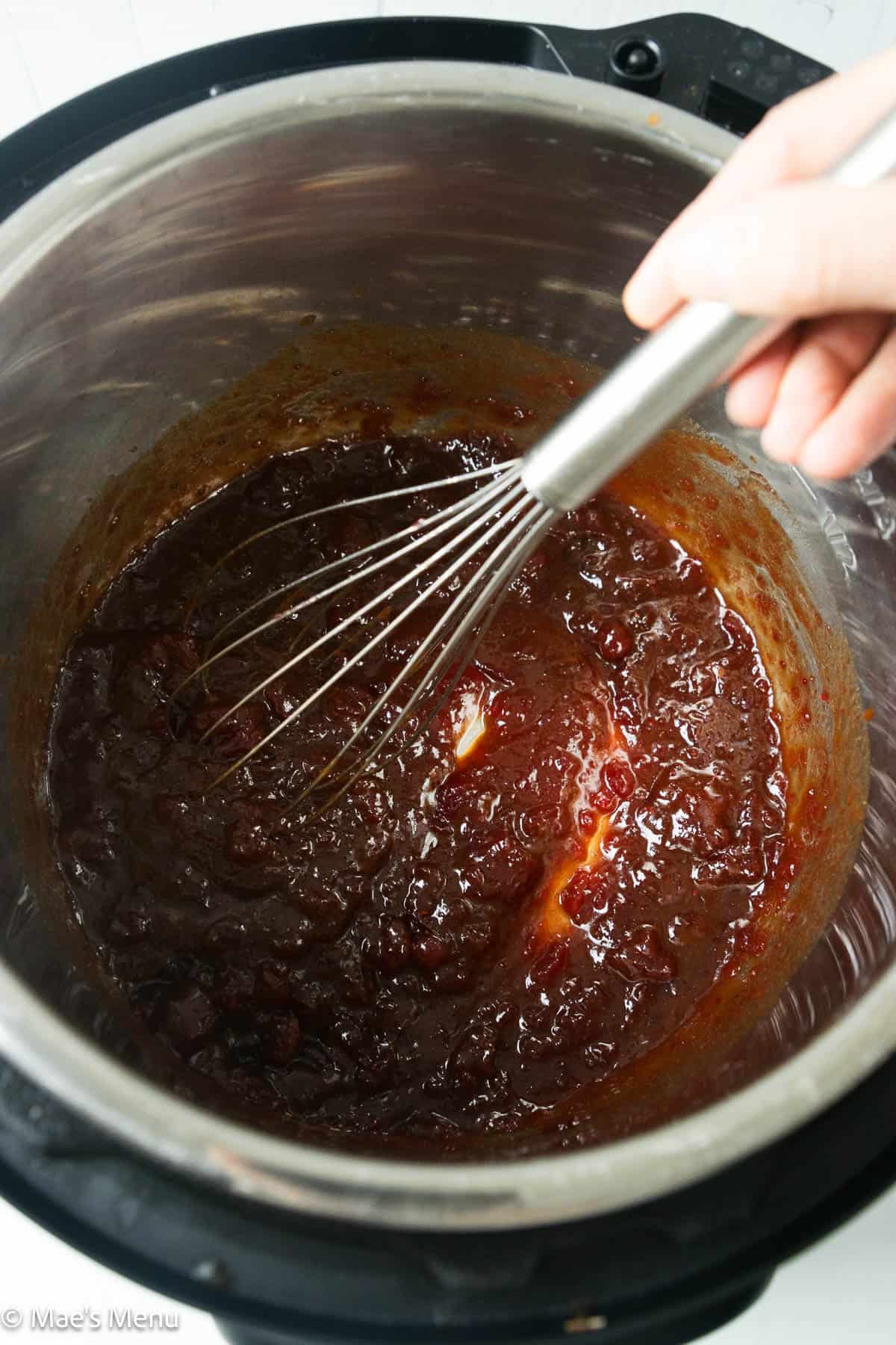 A hand whisking the cranberry meatball sauce in the instant pot.