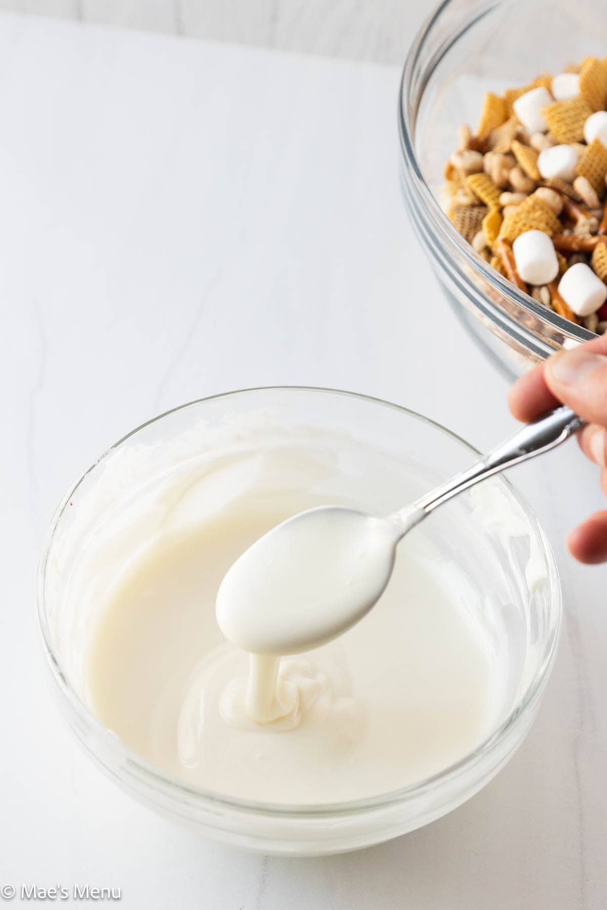 A spoon drizzling melted white chocolate over a mixing bowl.