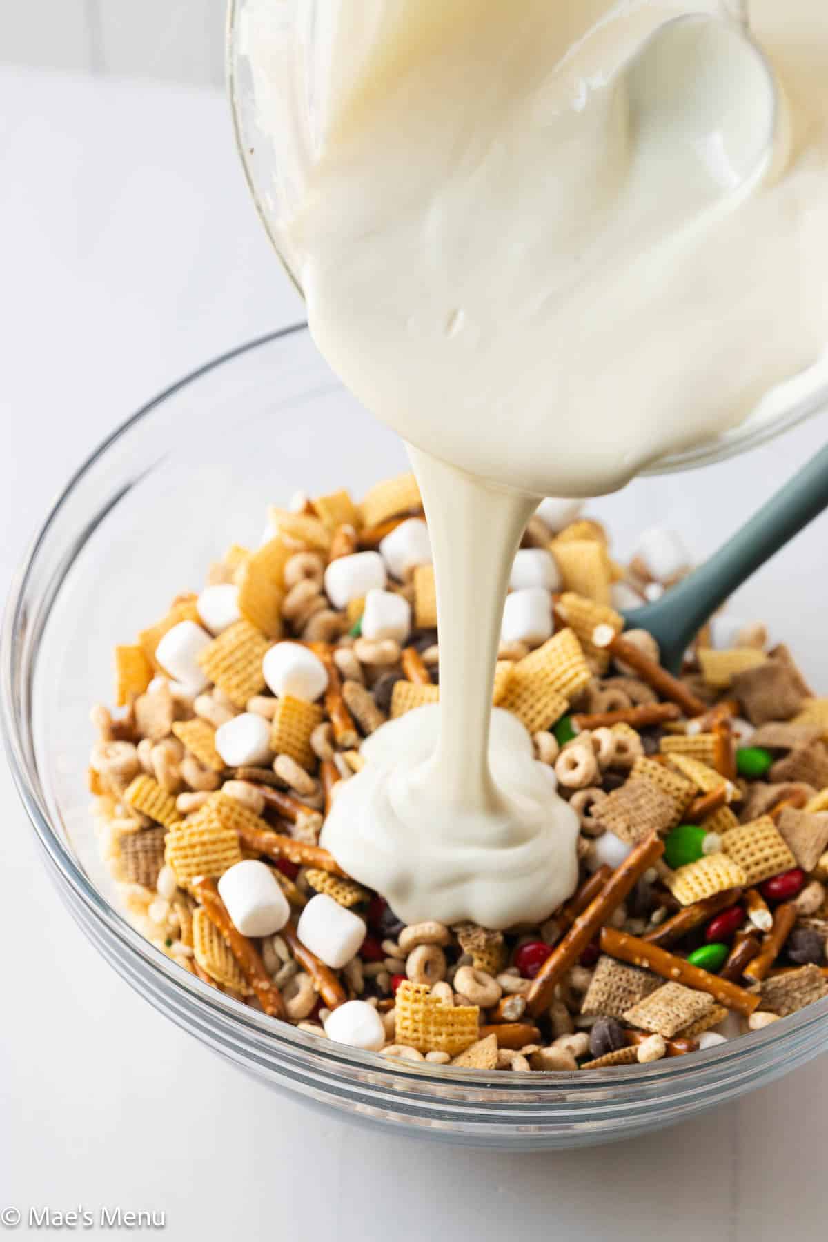 Pouring the melted white chocolate over the bowl of the christmas mix. 
