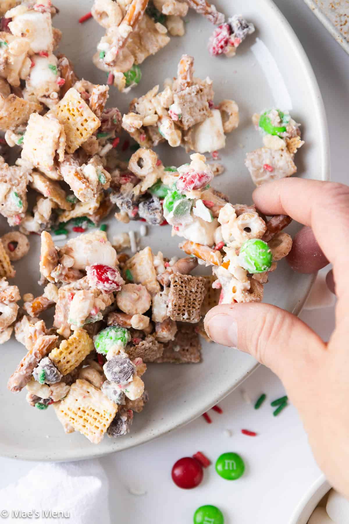 A hand taking a piece of the Christmas snack mix from the plate. 