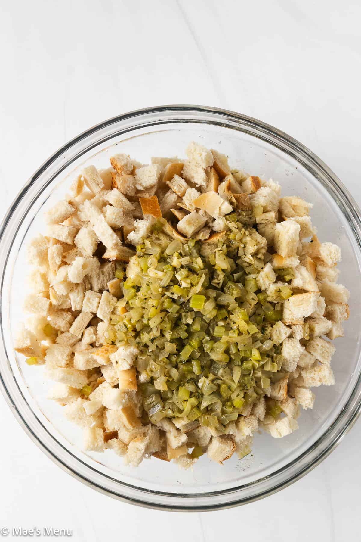 A mixing bowl of bread cubes and sauteed onions and celery.