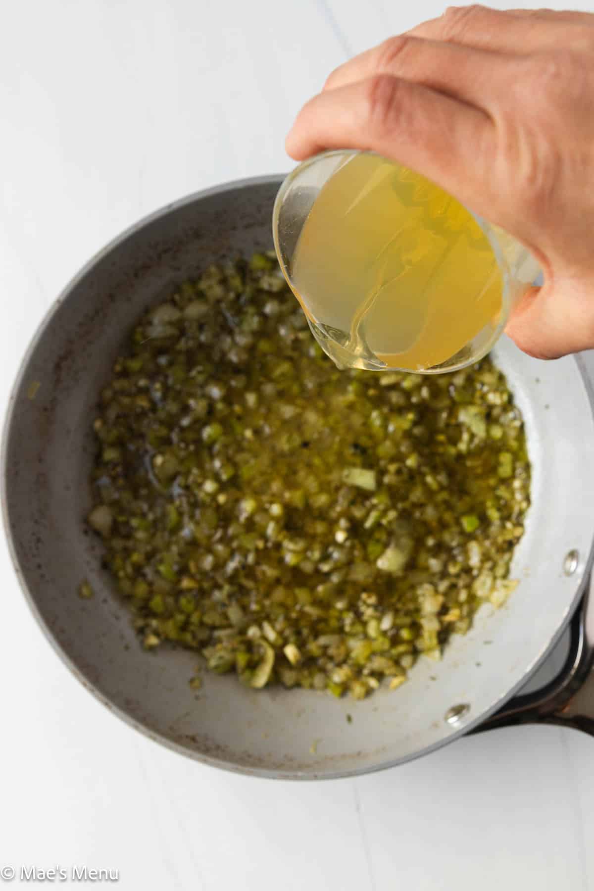 Adding chicken broth to the skillet of sauteed celery and onions.