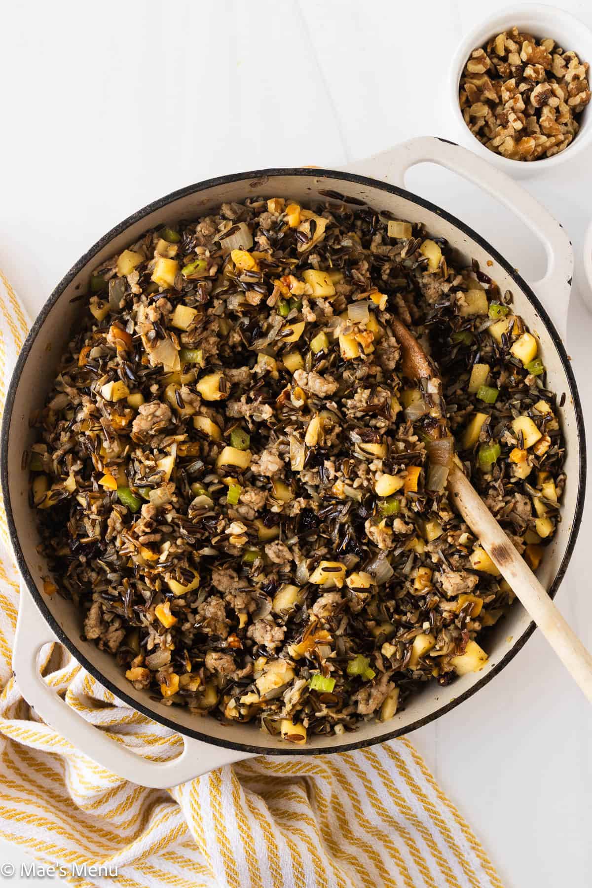 An overhead shot of a pan of wild rice stuffing with a wooden spoon next to a small dish of walnuts.