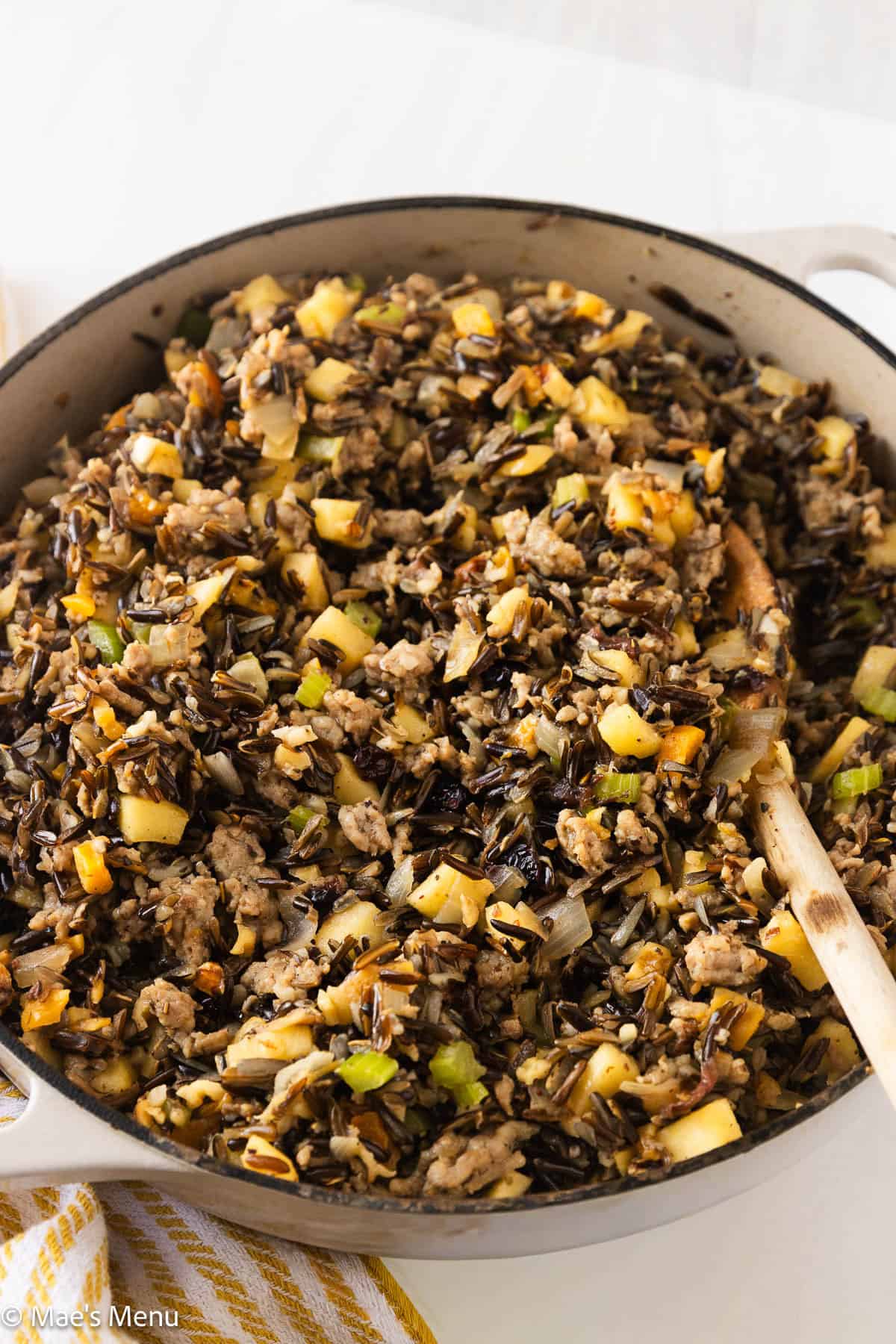 An angled shot of a pan of wild rice stuffing with a wooden spoon in it.
